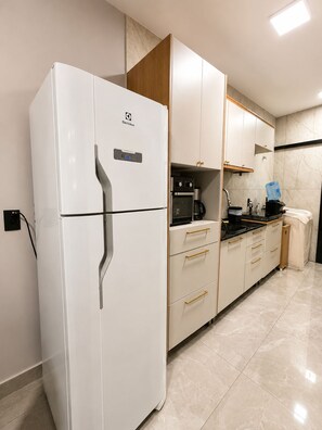 Una cocina moderna con un refrigerador blanco, armarios de madera, horno empotrado y una encimera con hervidor.