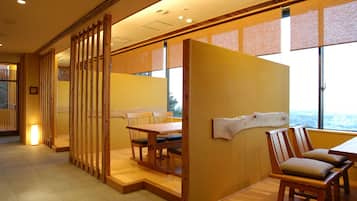 A room with a wooden partition, a dining table with chairs, and a view through large windows.