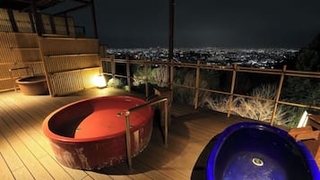 A rooftop terrace with a hot tub and a pool, overlooking a cityscape at night.