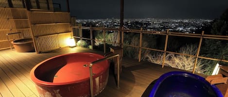 A rooftop terrace with a hot tub and a pool, overlooking a cityscape at night.