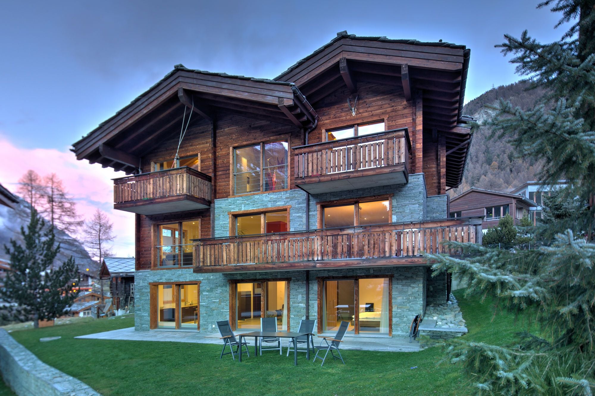 A multi-story wooden house with balconies, large windows, and a stone facade.