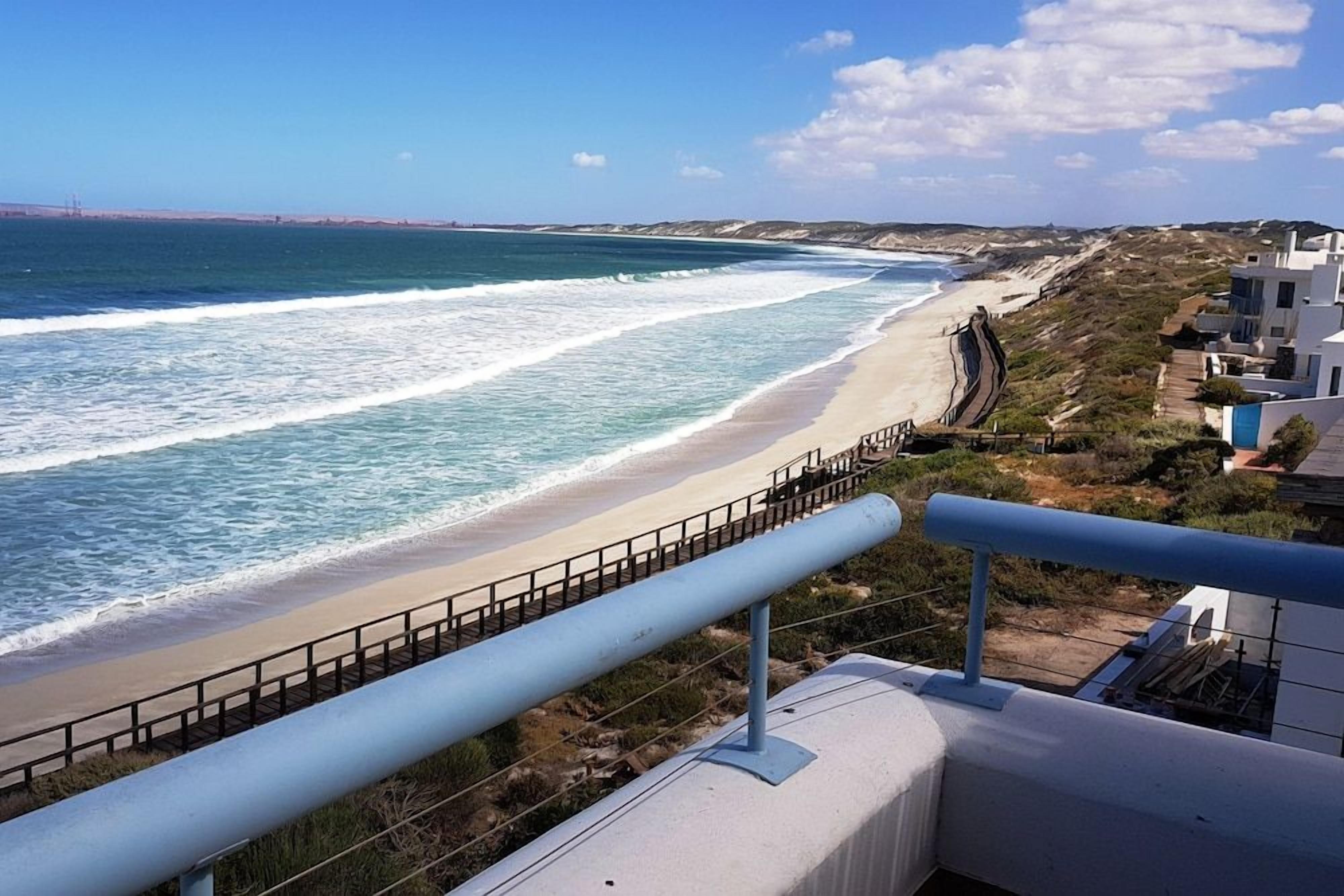 A coastal view with a beach, a railing, and buildings in the background.