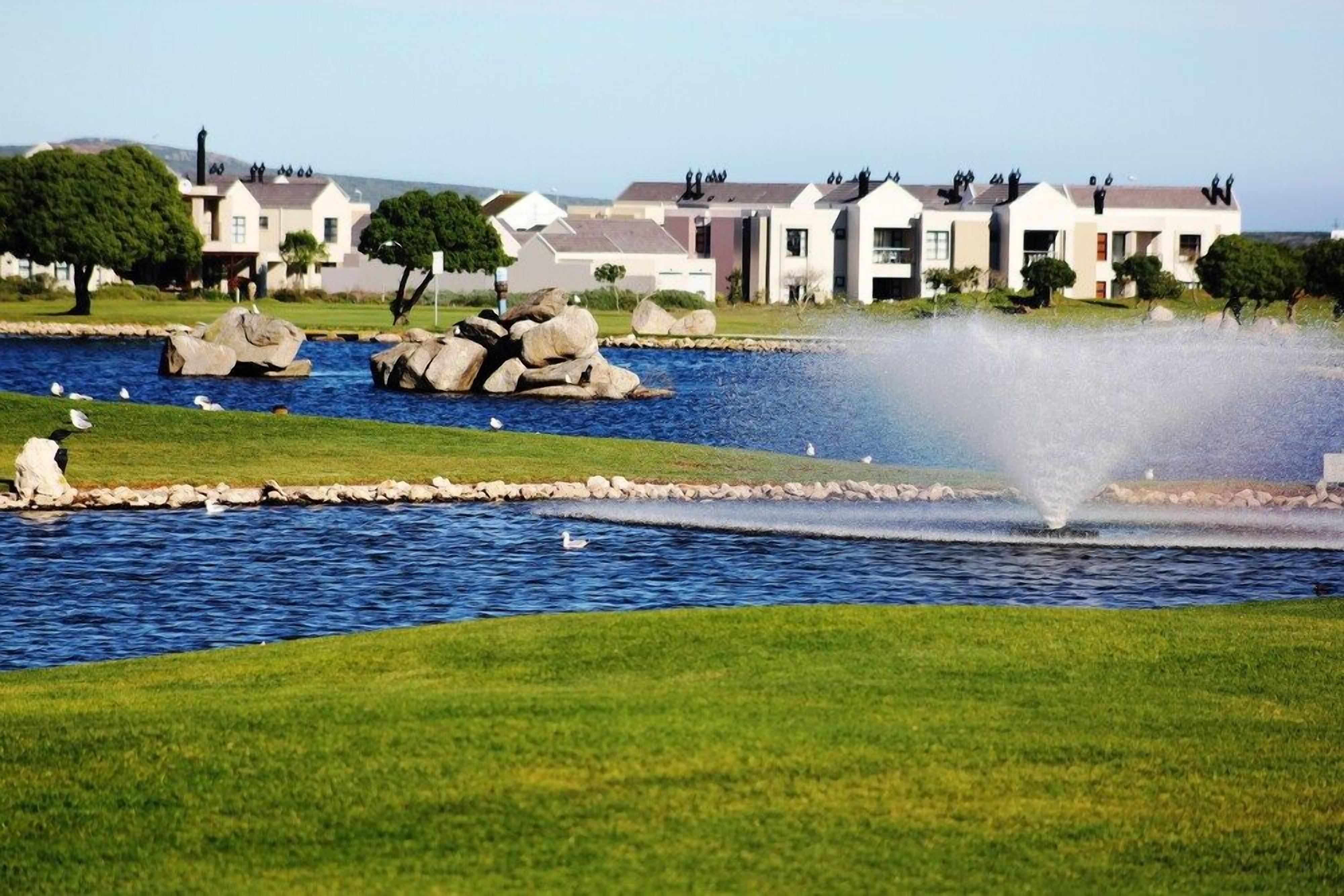 A residential area with a pond, a fountain, and houses with visible balconies.
