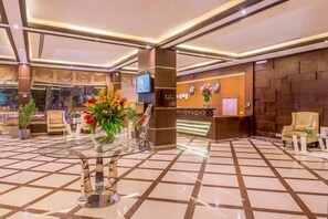 A hotel lobby with a reception desk, seating area, and a glass-top table with floral arrangements. - Al Muhaidb Residence Al Malaz 1 (Riyadh)