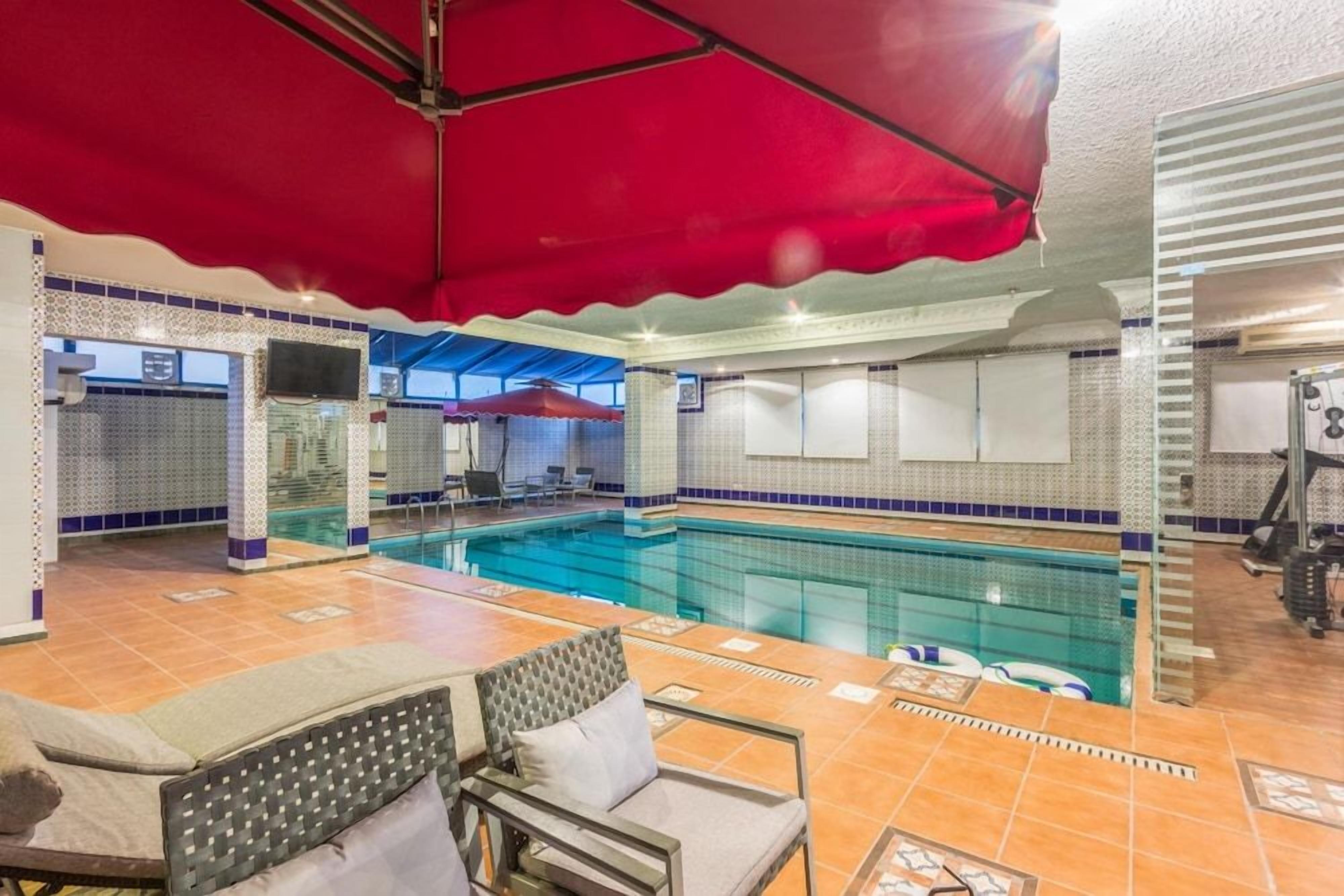 An indoor swimming pool with tiled walls, a red canopy, and lounge chairs.