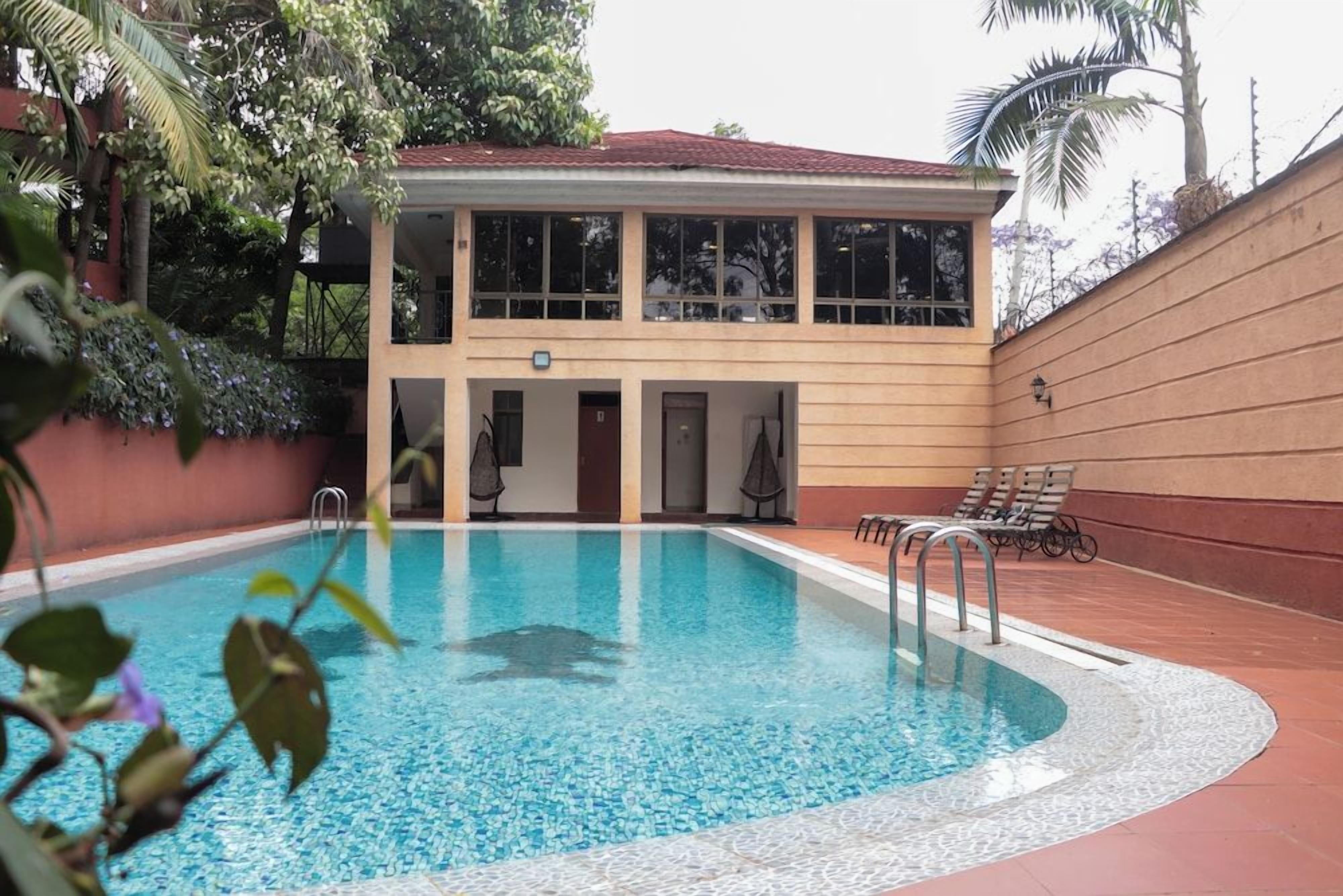 Una piscina con un edificio di due piani adiacente, dotato di una zona coperta con posti a sedere e una porta.