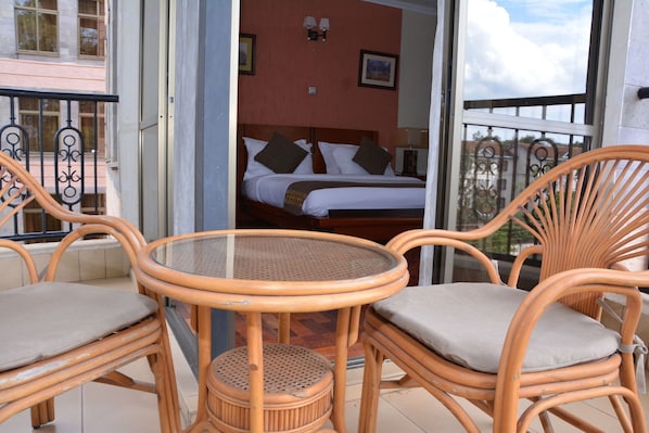 A balcony with wicker furniture, a bed with pillows, and a view of the outside. - Gemsuites Luxury Serviced Apartments (Nairobi)
