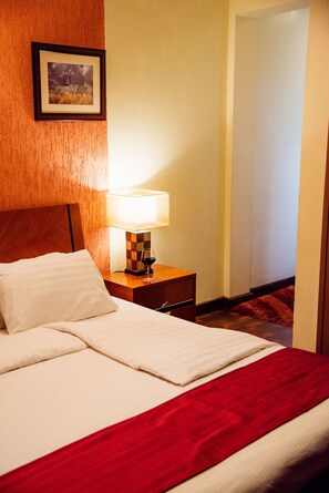 Una habitación de hotel con una cama, una mesita de noche con una lámpara y un cuadro en la pared.