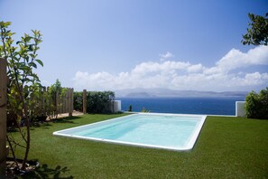 A rectangular pool with a clear blue poolside area, surrounded by well-maintained grass and a wooden fence. - Diadema Villa (Naxos)