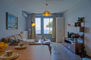 A living room with a view of the sea, a dining area with a table set for two, and a bookshelf with books and decorative items. - Diadema Villa (Naxos)