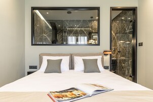 Habitación de hotel con una cama grande, un espejo encima y una puerta a la derecha.