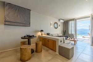 Un espacio habitable moderno con una isla de cocina, taburetes de madera, un sofá y vistas al exterior.