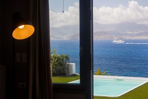 A view from a room with a large window overlooking a swimming pool and the sea.