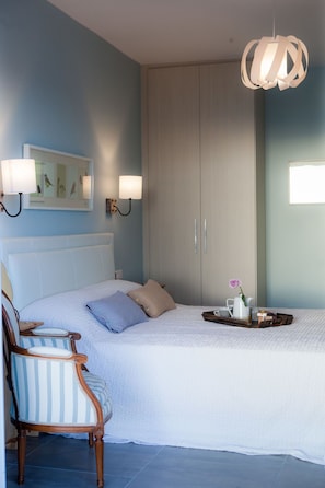A bedroom with a bed, a chair, a bedside table with a vase, and a hanging light fixture. - Diadema Villa (Naxos)