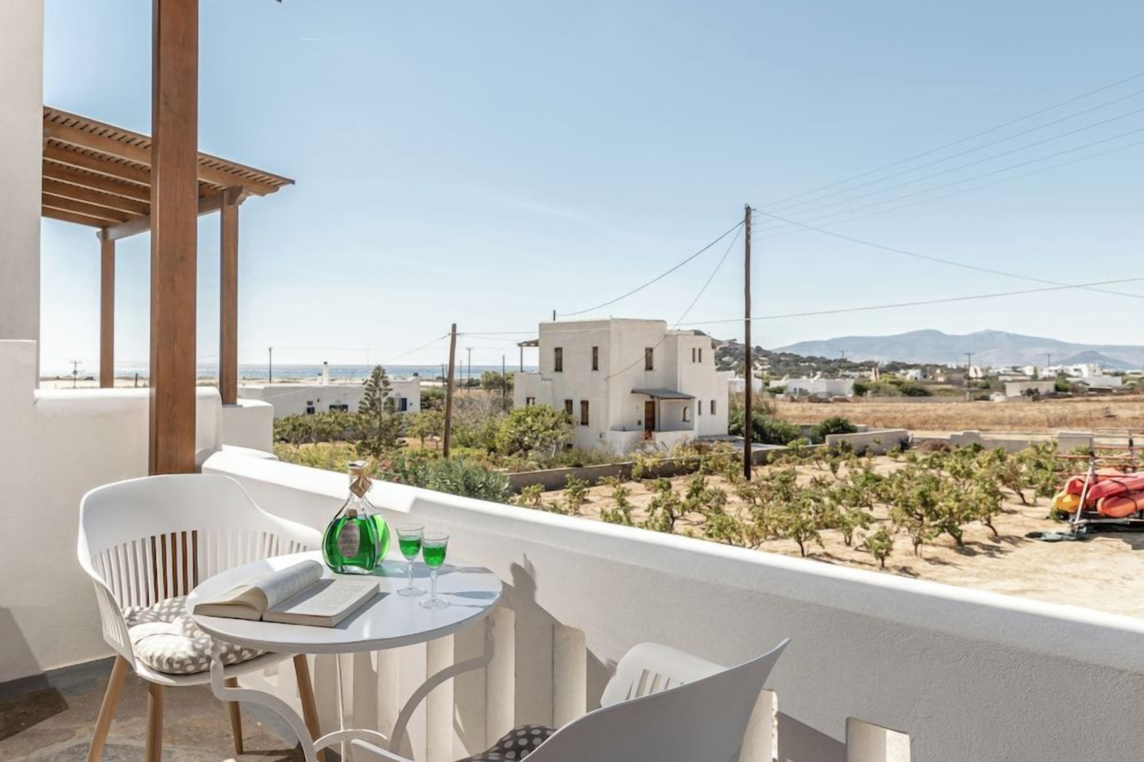 Un balcon avec une table et des chaises, donnant sur un paysage composé de bâtiments et d’un vignoble.