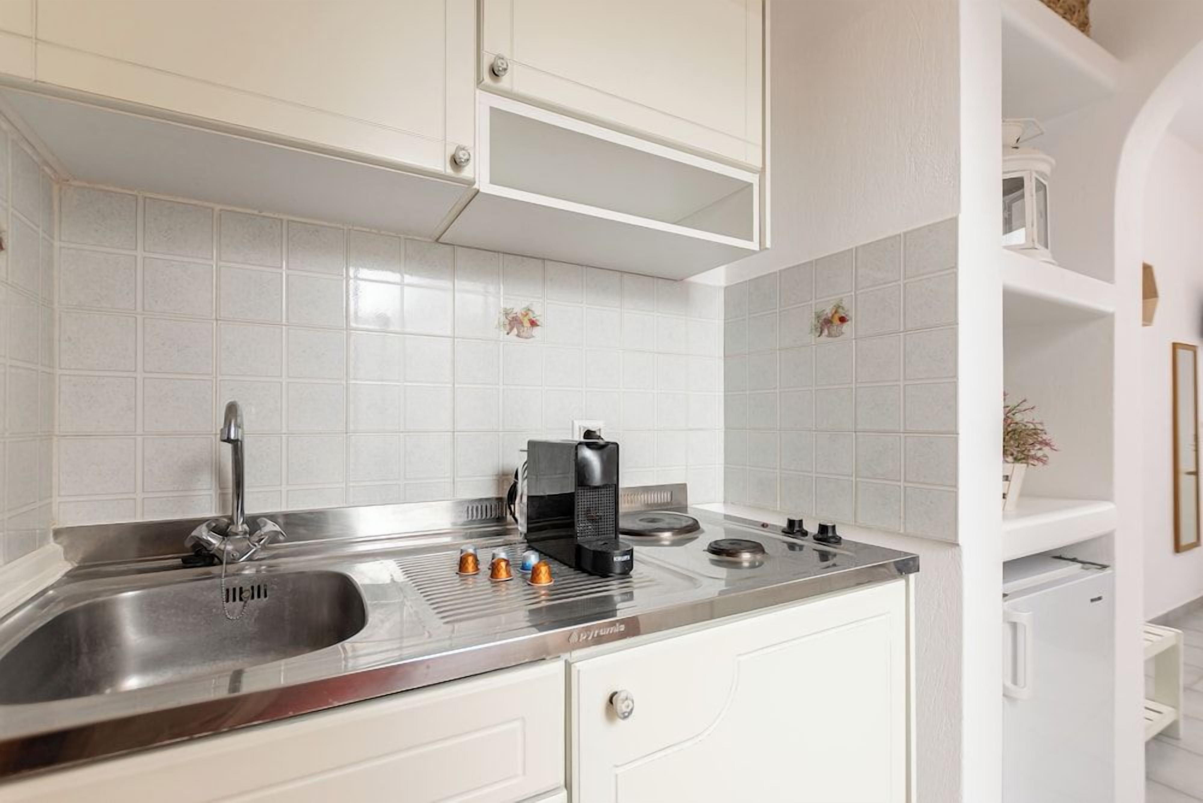 A kitchen with white cabinets, a stainless steel sink, and a coffee maker.