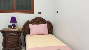 A bedroom with a single bed, a nightstand, a lamp, and a window with blinds.
