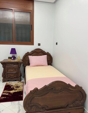 Quarto com uma cama de solteiro, mesa de cabeceira, luminária e janela com persianas.