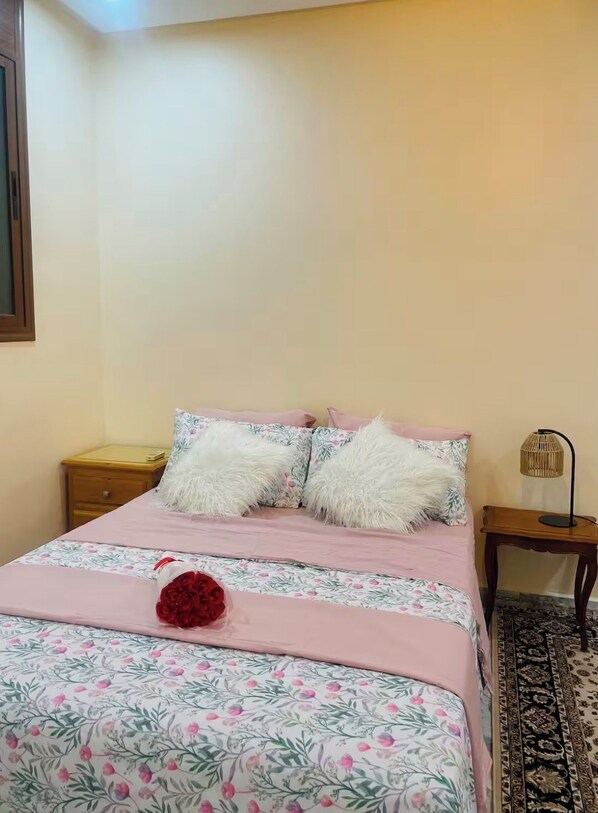 A bedroom with a bed, a nightstand, a lamp, and a patterned rug.