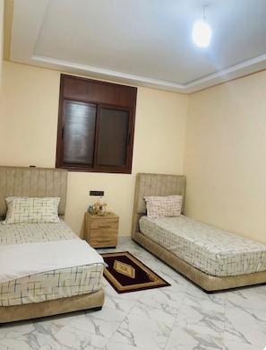 Quarto com duas camas, mesa de cabeceira, janela e luminária de teto.