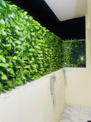 A corridor with a green leafy wall, a window with a view of trees, and a tiled floor.