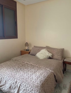 Quarto com uma cama, mesa de cabeceira, abajur e janela.