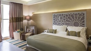 Ein Hotelzimmer mit einem großen Bett, einem Sessel, einem Nachttisch und einem dekorativen Kopfteil.