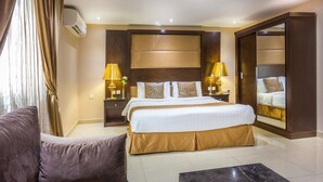 Ein Hotelzimmer mit einem großen Bett, zwei Nachttischen mit Lampen, einem Sofa, einem Couchtisch und einem Spiegel.