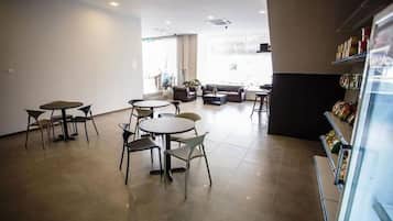 A spacious indoor area with multiple seating arrangements including tables and chairs, a sofa, and a counter with food items.