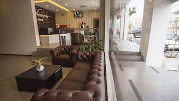 A hotel lobby with a reception desk, seating area, and a view of the street.