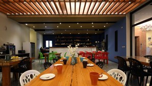 Uma sala de jantar com uma mesa de madeira comprida, várias cadeiras e uma cozinha ao fundo.