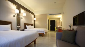 Quarto de hotel com duas camas, um sofá, uma televisão e um banheiro visível ao fundo.
