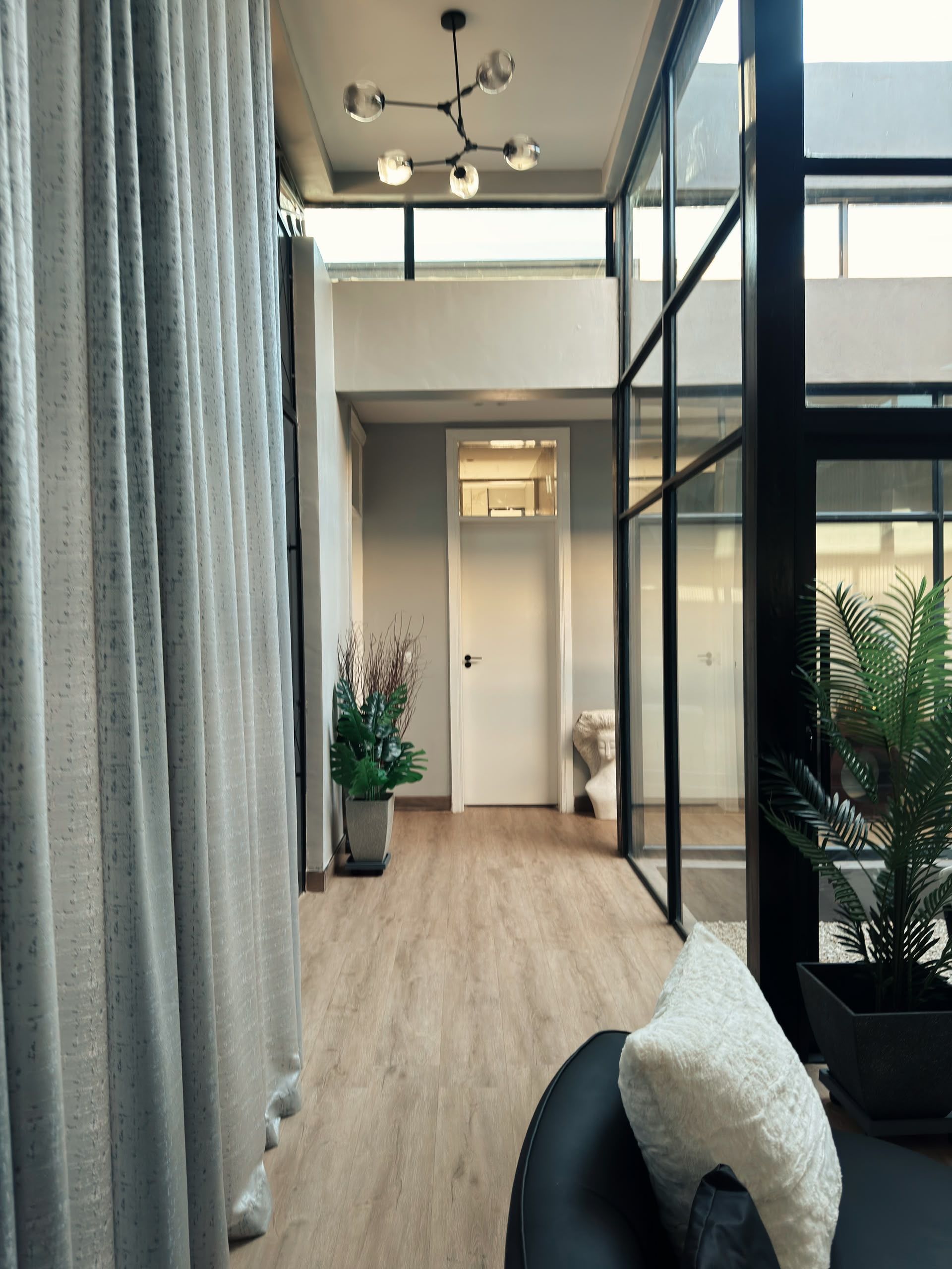 Ein modernes Interieur mit Deckenventilator, einer T ür zu einem anderen Raum und Blick durch große Fenster.