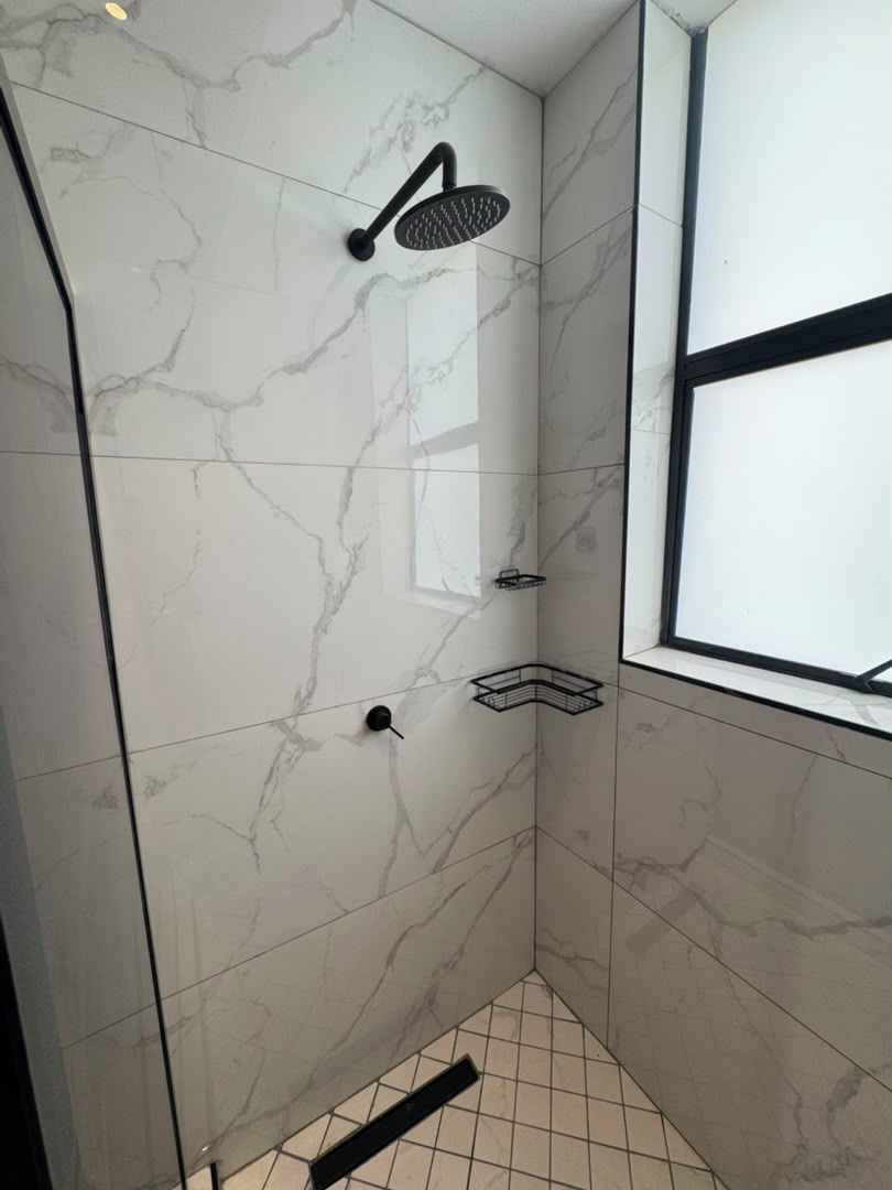 Une douche équipée d’un pommeau de douche à main, d’une fenêtre et d’une étagère d’angle.