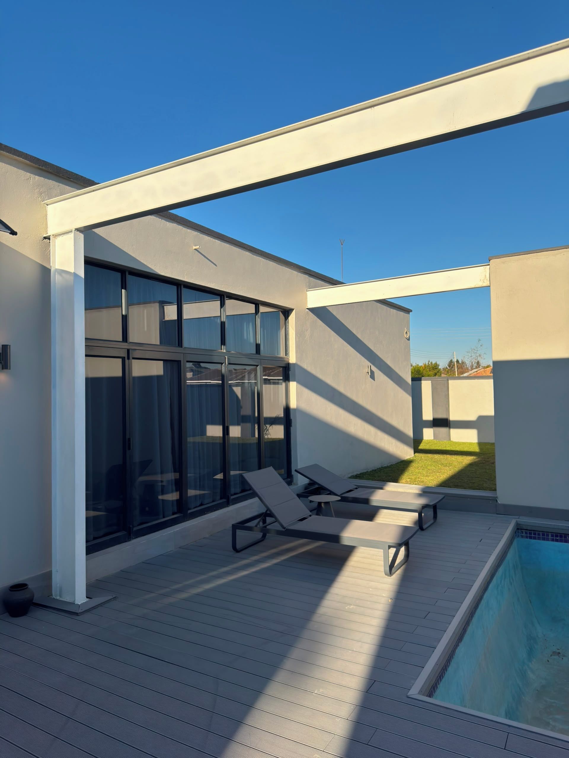Un espace piscine extérieur moderne, doté de chaises longues et d’un patio fermé par des baies vitrées.
