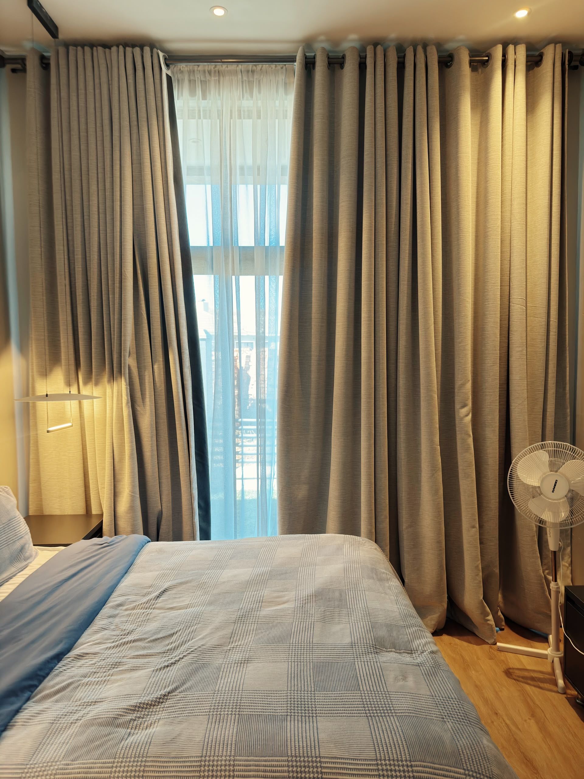 A bedroom with a bed, curtains, a fan, and a window.