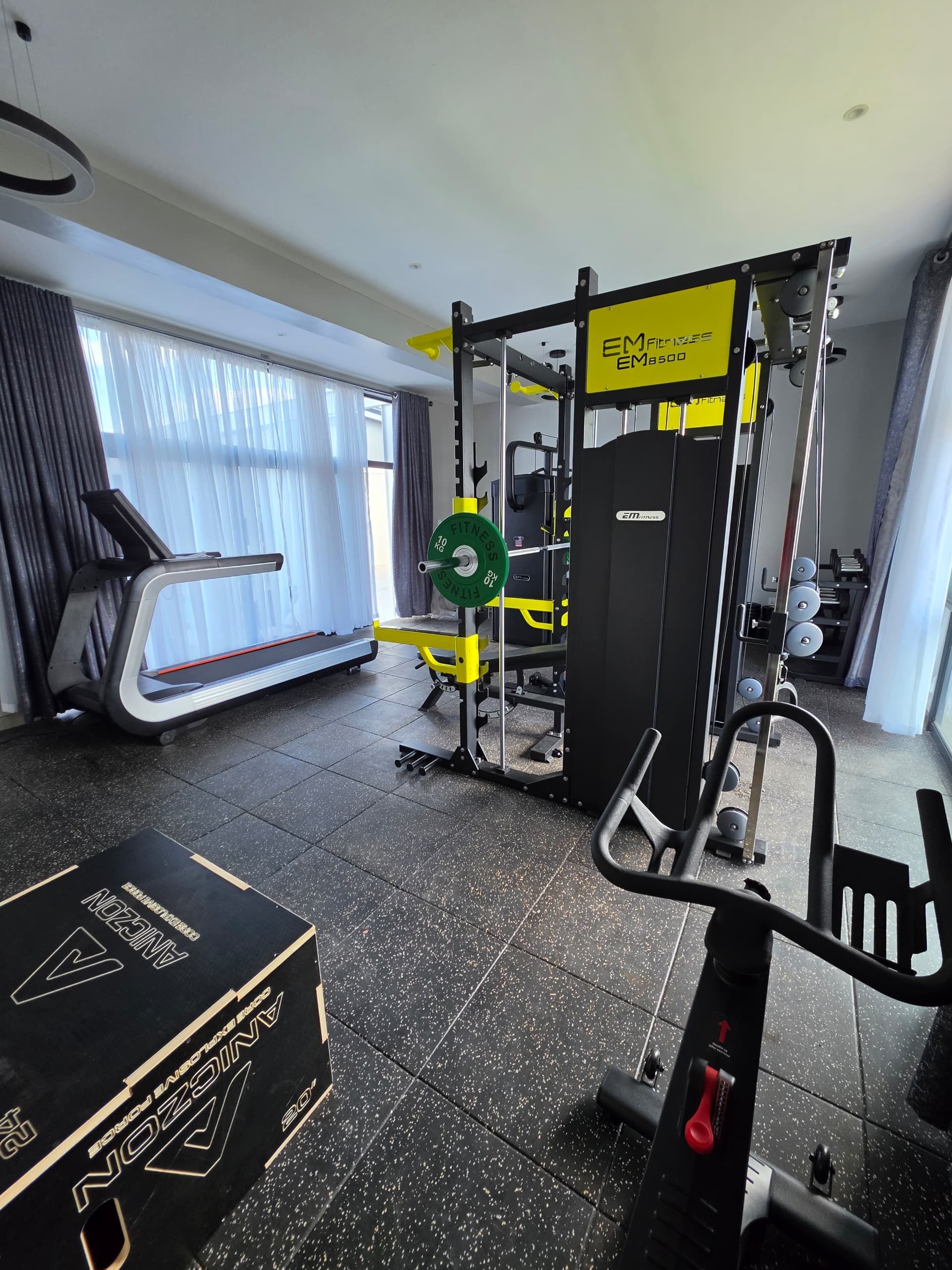 Un gimnasio con equipo de ejercicio, cinta de correr y zona de levantamiento de pesas.
