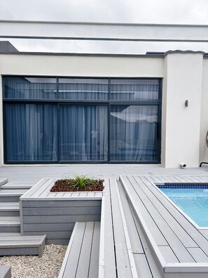 Une terrasse extérieure moderne avec une piscine, un jardinier avec des plantes et une grande porte coulissante.