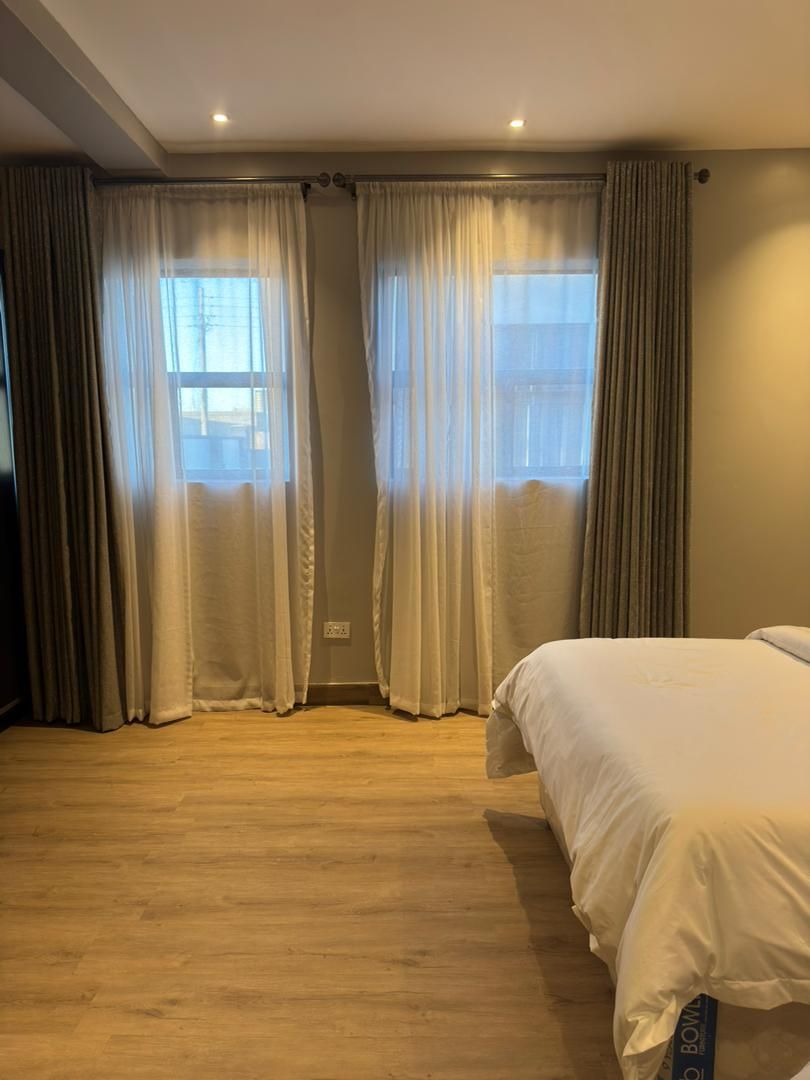 Un dormitorio con cama, suelo de madera y ventana con cortinas.