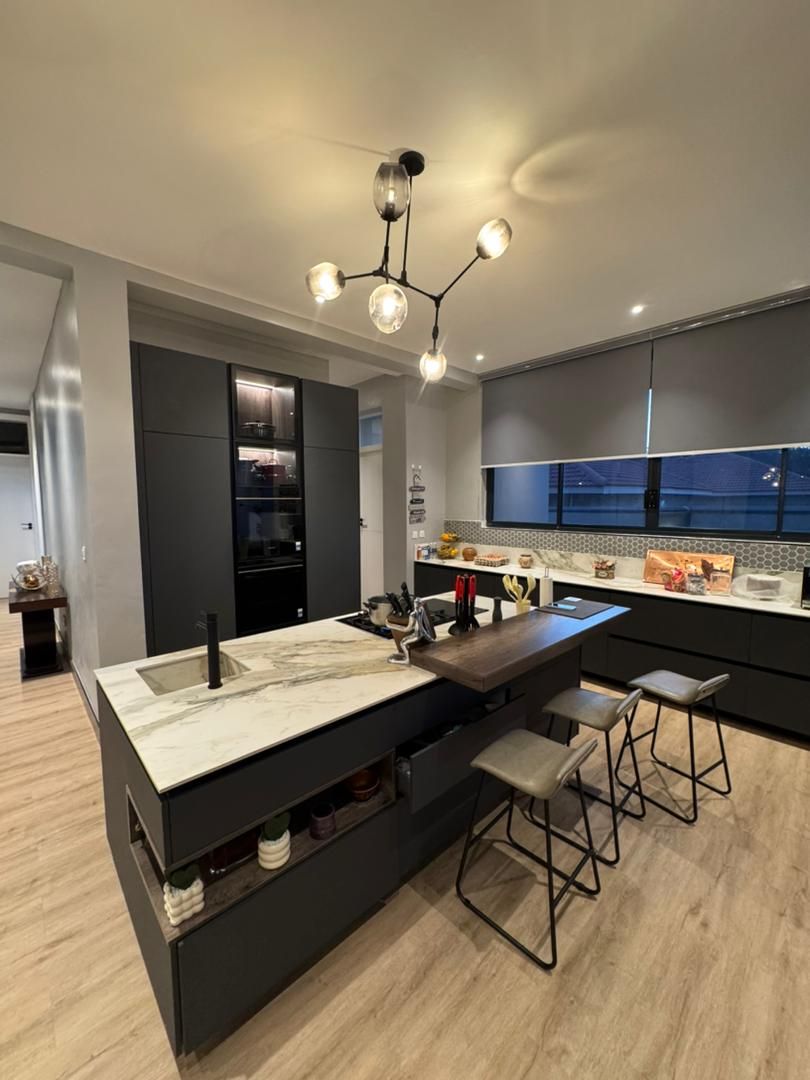 Una cocina moderna con una isla central, taburetes de bar y una lámpara colgante.