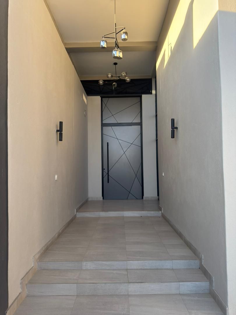 Un couloir avec une porte ornée d’un motif géométrique, un escalier et des luminaires suspendus.