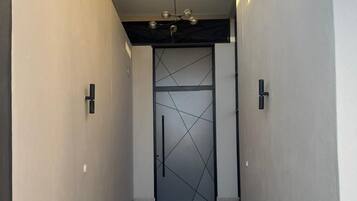 Un couloir avec une porte ornée d’un motif géométrique, un escalier et des luminaires suspendus.