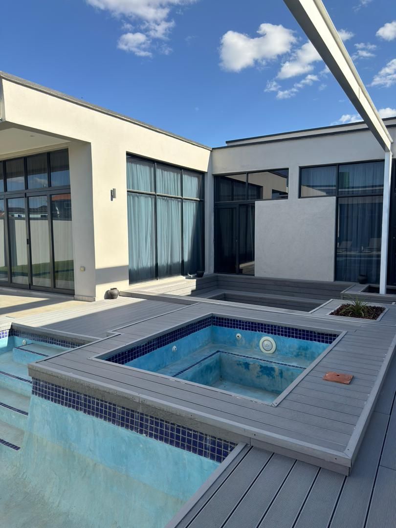 A modern outdoor swimming pool with a wooden deck and a covered area.