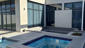 A modern outdoor swimming pool with a wooden deck and a covered area.