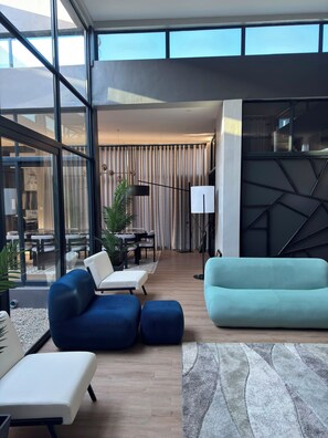 Sala de estar moderna com sofá, cadeiras e área de jantar visível por grandes janelas.