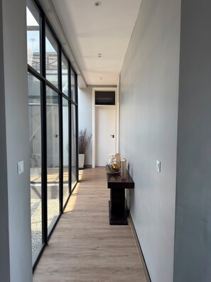 A modern hallway with large glass doors leading to an outdoor area, a dark wooden floor, and a small table with decorative items.