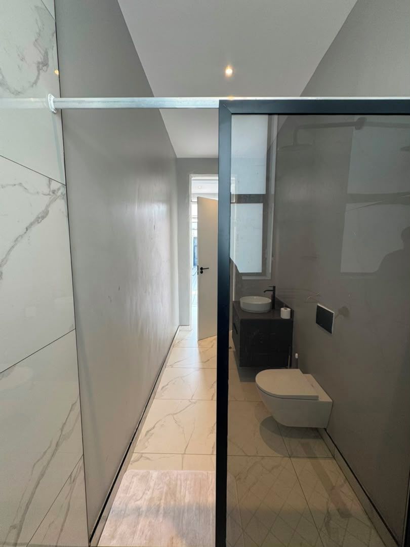 A modern bathroom with a glass shower enclosure, a toilet, and a sink.