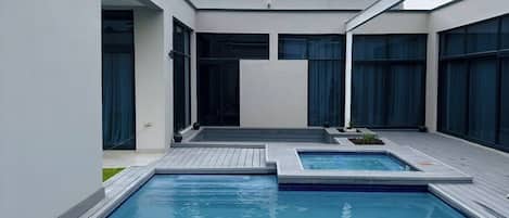 Una piscina moderna de forma rectangular con un jacuzzi pequeño en el centro.