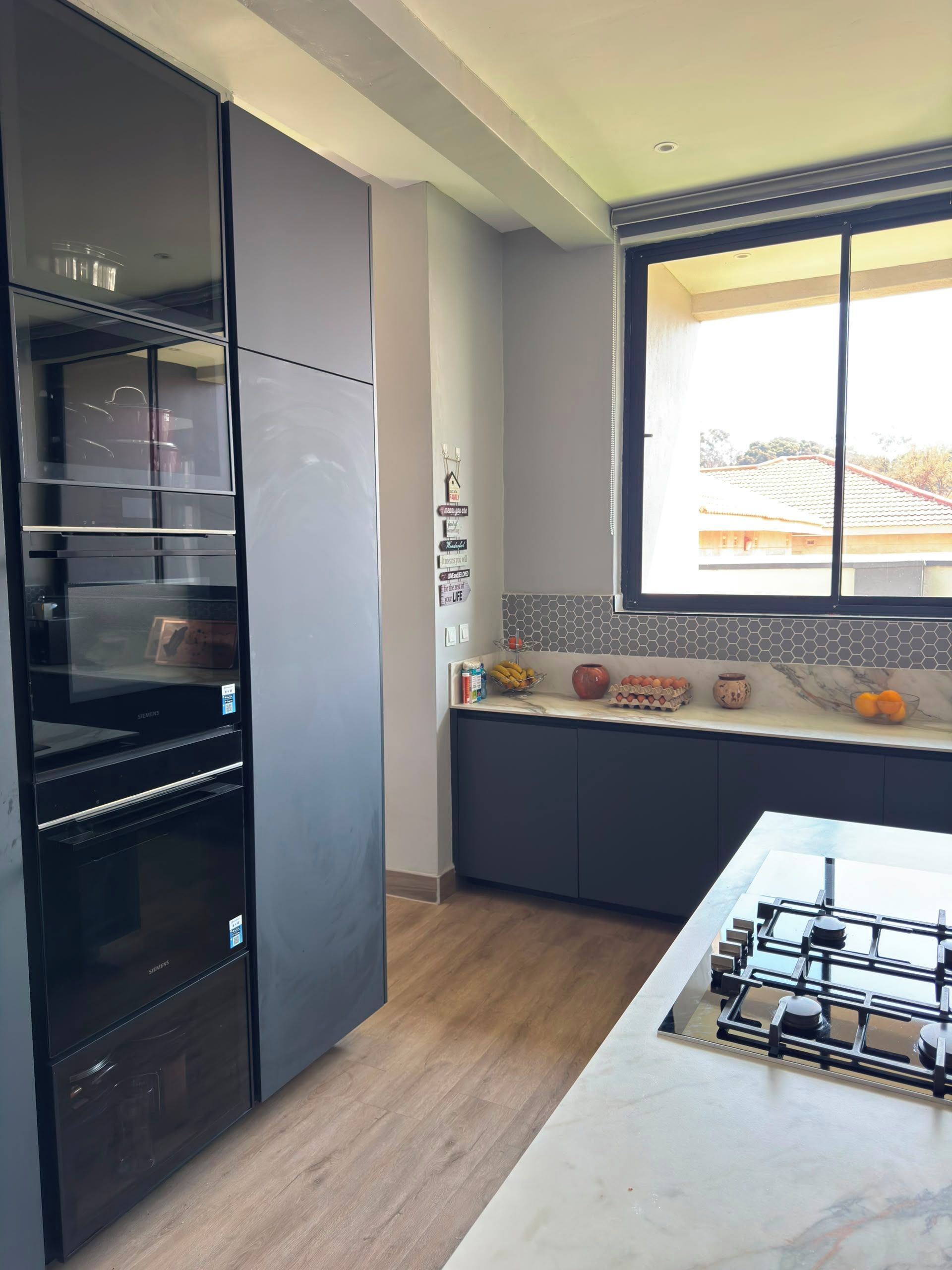 Une cuisine moderne équipée d’un four encastré, d’une cuisinière à gaz et d’une fenêtre donnant sur une maison.