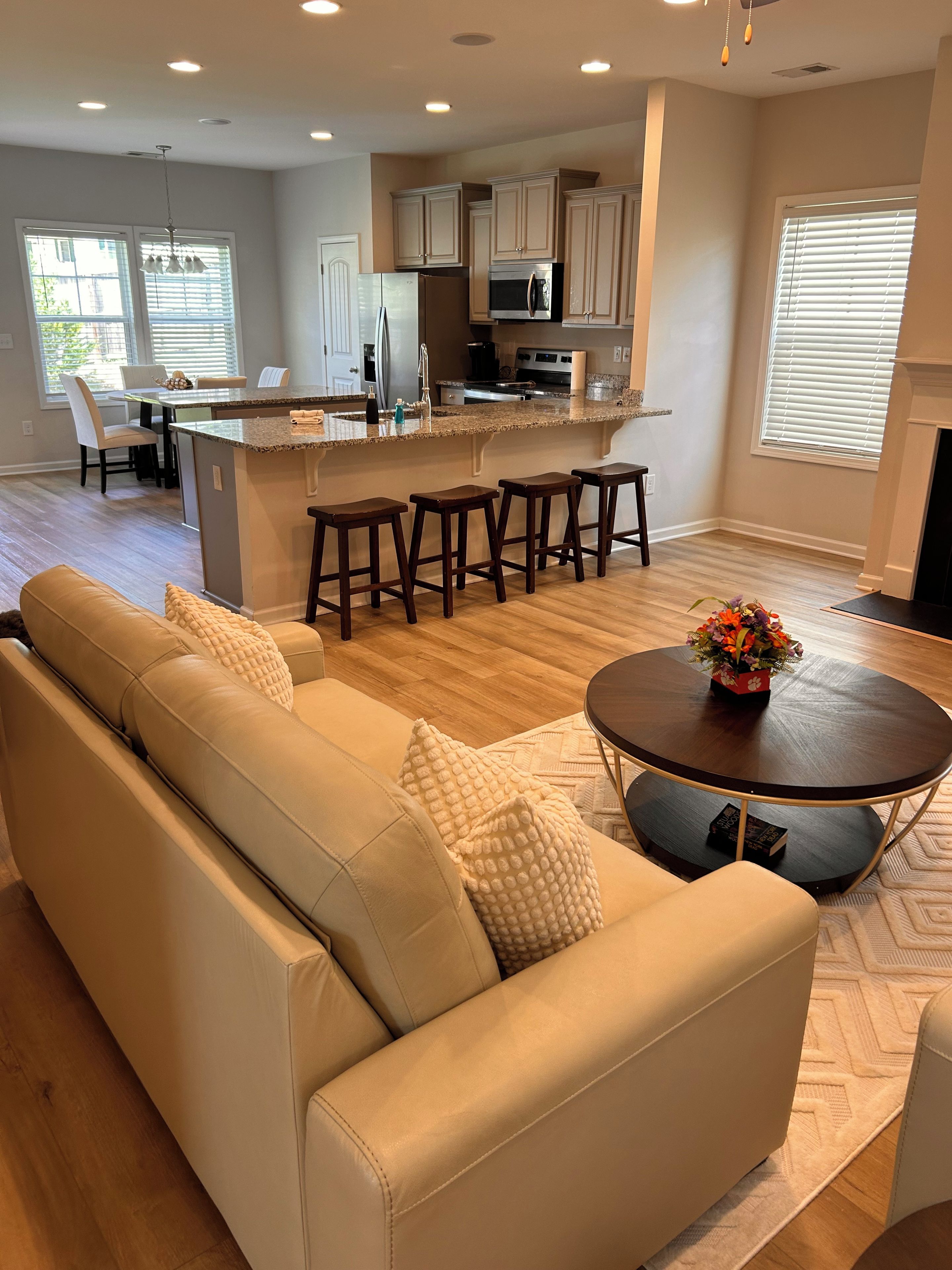 A modern living room with a beige sofa, a round coffee table, and a kitchen area with a central island and bar stools.